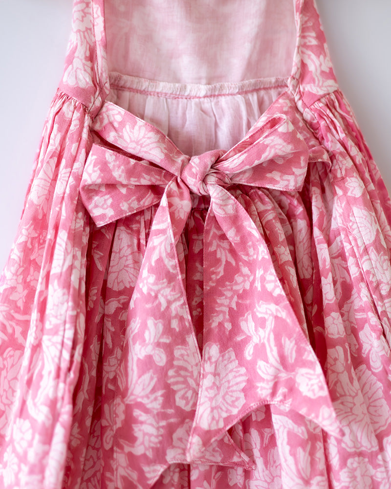 Girl on the beach in a summery pink dress. Light pink hand block printed floral summer halter neck dress made with 100% soft and breathable mulmul cotton with adjustable tie ups and elastication. Lined with mul. Upcycled hair clips in kora cotton on the little girls hair.