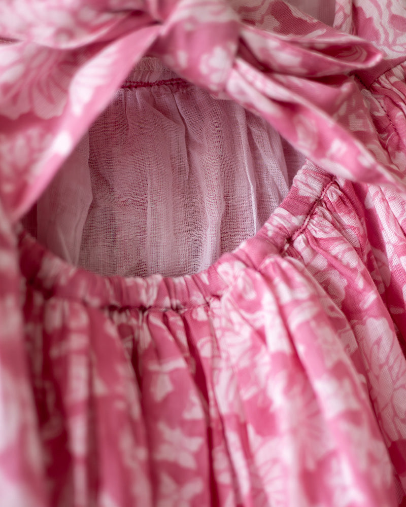 Girl on the beach in a summery pink dress. Light pink hand block printed floral summer halter neck dress made with 100% soft and breathable mulmul cotton with adjustable tie ups and elastication. Lined with mul. Upcycled hair clips in kora cotton on the little girls hair.