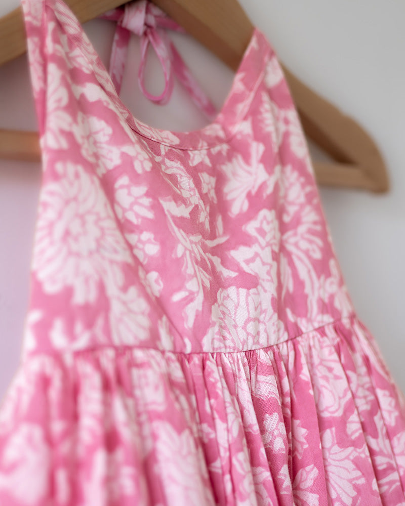 Girl on the beach in a summery pink dress. Light pink hand block printed floral summer halter neck dress made with 100% soft and breathable mulmul cotton with adjustable tie ups and elastication. Lined with mul. Upcycled hair clips in kora cotton on the little girls hair.