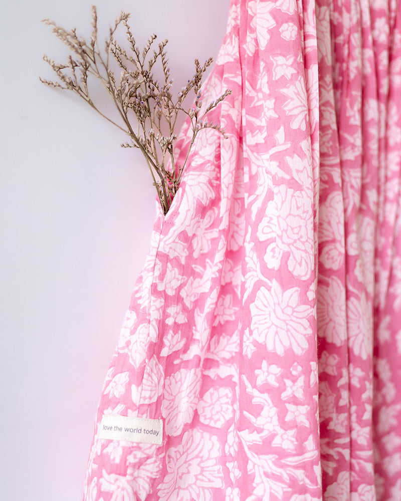 Girl on the beach in a summery pink dress. Light pink hand block printed floral summer halter neck dress made with 100% soft and breathable mulmul cotton with adjustable tie ups and elastication. Lined with mul. Upcycled hair clips in kora cotton on the little girls hair.