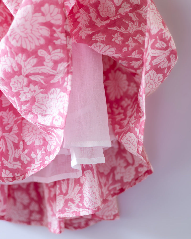 Girl on the beach in a summery pink dress. Light pink hand block printed floral summer halter neck dress made with 100% soft and breathable mulmul cotton with adjustable tie ups and elastication. Lined with mul. Upcycled hair clips in kora cotton on the little girls hair.