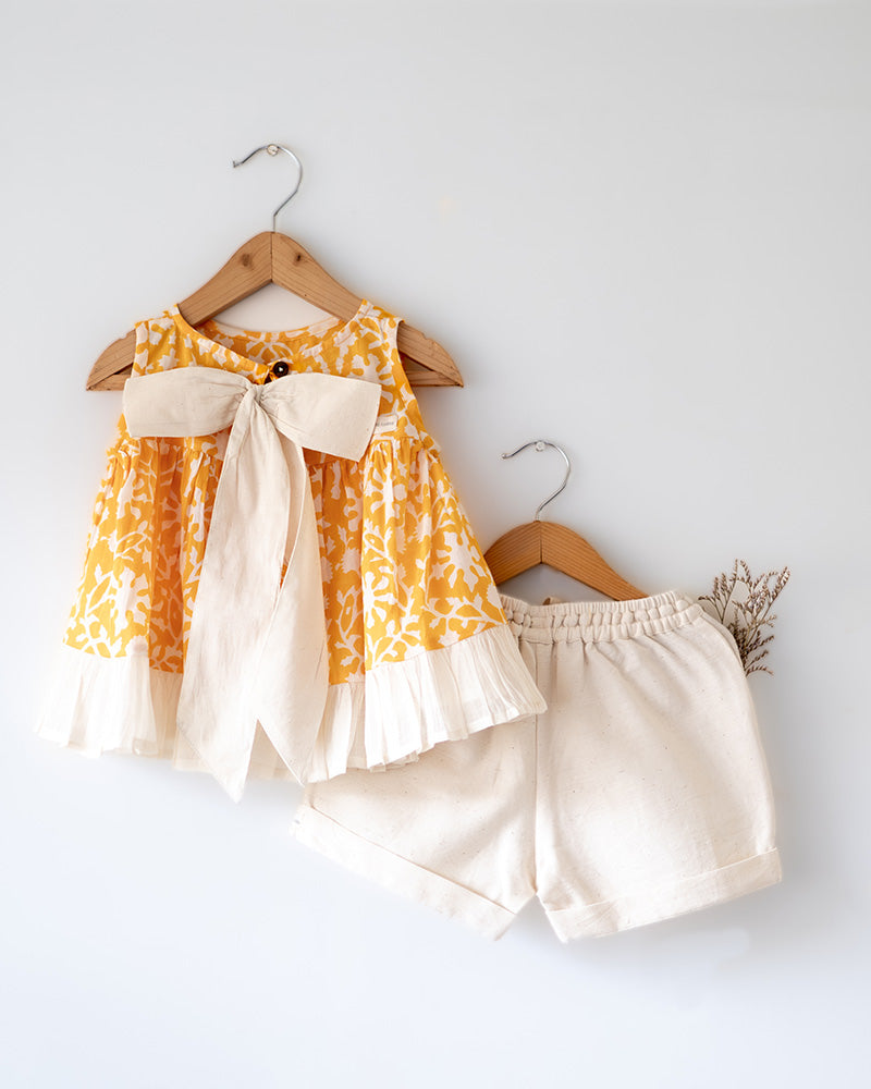 Coord set for girls with a yellow handblock printed voluminous flared style cotton top and kora handwoven shorts. Made with 100% soft and breathable cotton hand block printed in Jaipur, Rajasthan. The top is kedia styled flared with tie ups at the back for ease of wear. Shorts have a soft elasticated band on waist and come with pockets.