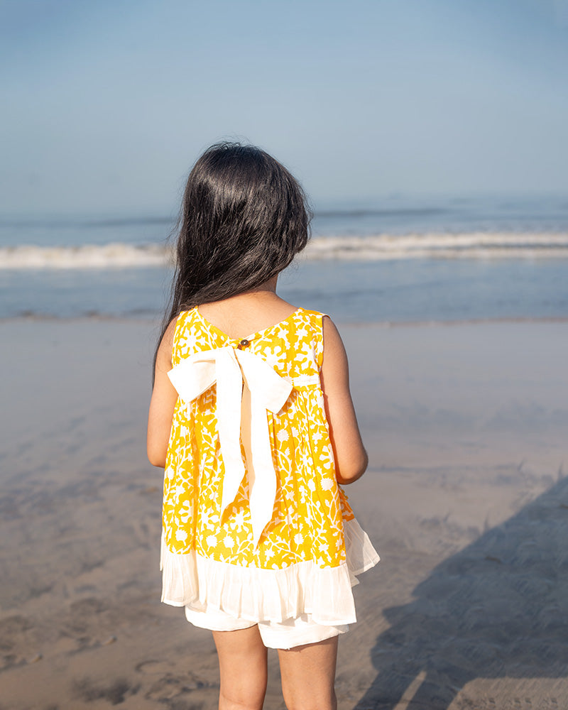 Coord set for girls with a yellow handblock printed voluminous flared style cotton top and kora handwoven shorts. Made with 100% soft and breathable cotton hand block printed in Jaipur, Rajasthan. The top is kedia styled flared with tie ups at the back for ease of wear. Shorts have a soft elasticated band on waist and come with pockets.