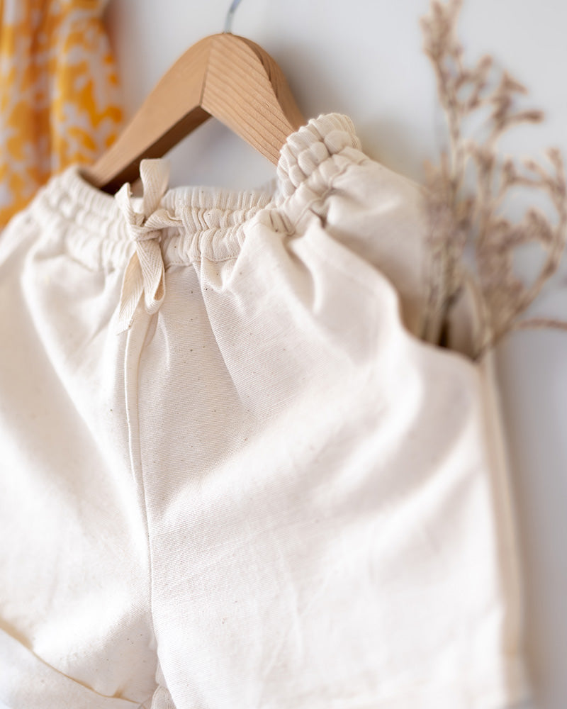 Coord set for girls with a yellow handblock printed voluminous flared style cotton top and kora handwoven shorts. Made with 100% soft and breathable cotton hand block printed in Jaipur, Rajasthan. The top is kedia styled flared with tie ups at the back for ease of wear. Shorts have a soft elasticated band on waist and come with pockets.