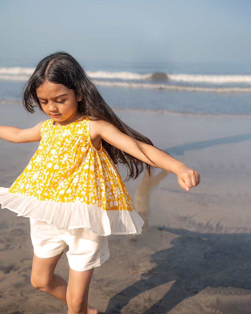 Coord set for girls with a yellow handblock printed voluminous flared style cotton top and kora handwoven shorts. Made with 100% soft and breathable cotton hand block printed in Jaipur, Rajasthan. The top is kedia styled flared with tie ups at the back for ease of wear. Shorts have a soft elasticated band on waist and come with pockets.