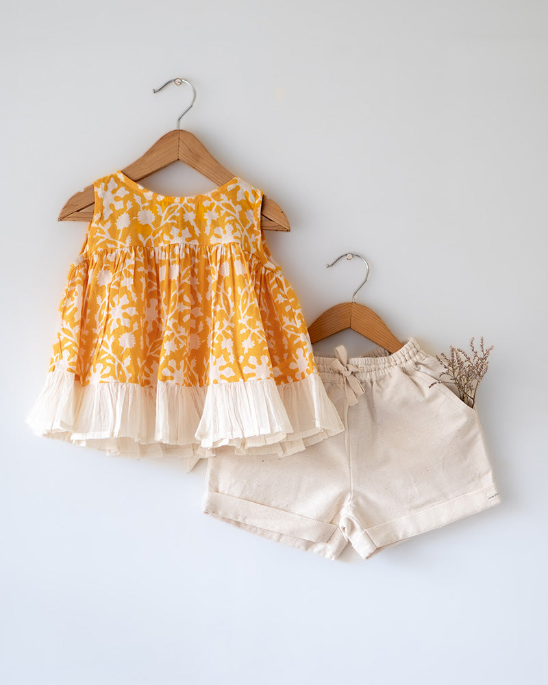 Coord set for girls with a yellow handblock printed voluminous flared style cotton top and kora handwoven shorts. Made with 100% soft and breathable cotton hand block printed in Jaipur, Rajasthan. The top is kedia styled flared with tie ups at the back for ease of wear. Shorts have a soft elasticated band on waist and come with pockets.