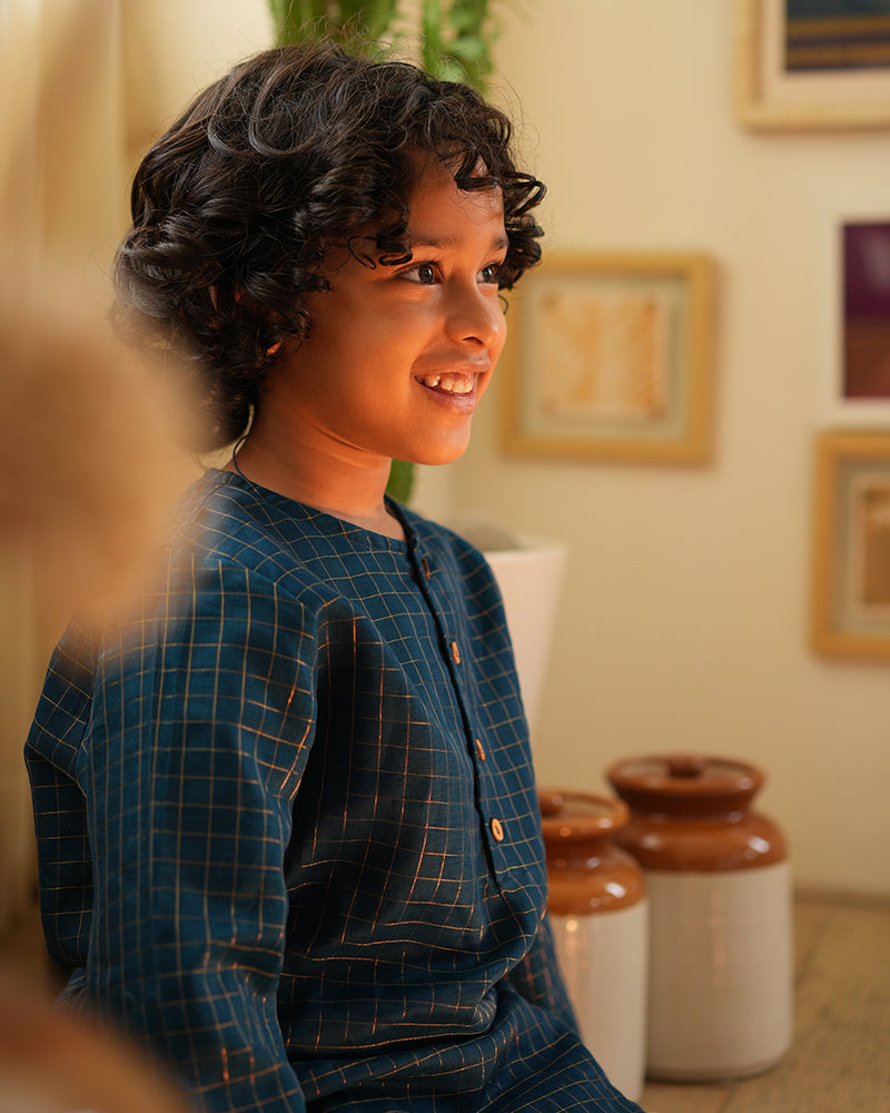 A Boy wearing a dark teal blue Indian festive Kurta with golden checks made with Handwoven cotton silk fabric woven by artisans in Maheshwar Madhya Pradesh.