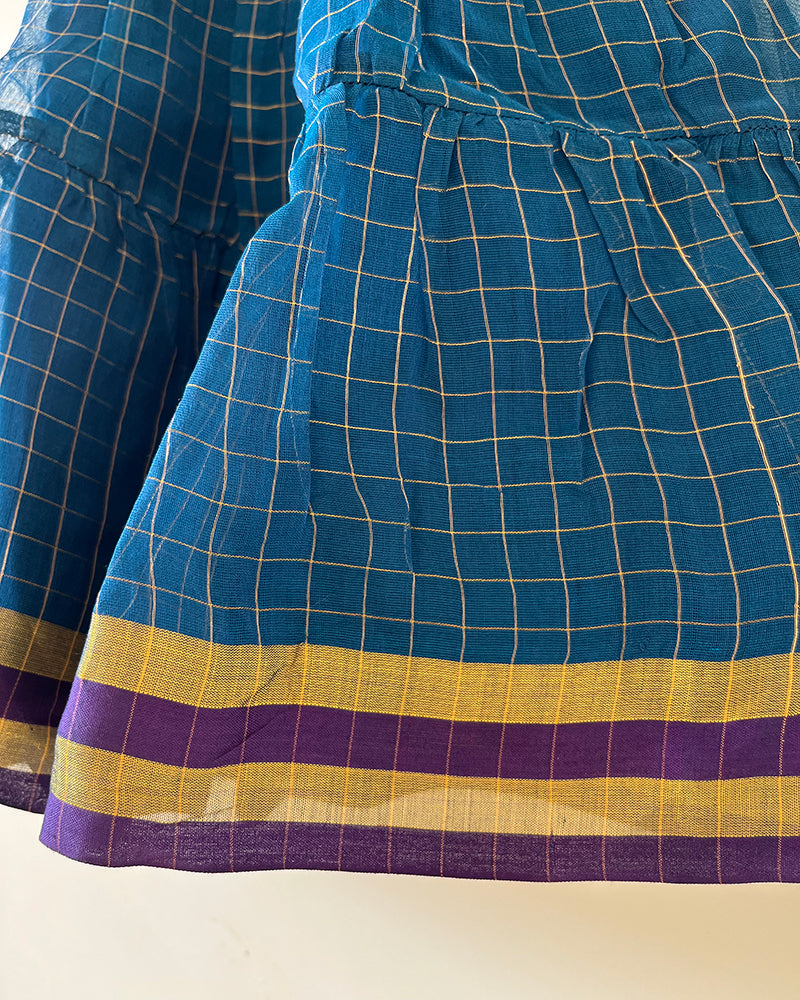 A deep teal blue sleeveless tiered dress with golden checks for infants in handwoven cotton silk by artisans in Maheshwar Madhya Pradesh. Perfect for festivities like Navratri, diwali, Dussehra, dushehra, bhai dooj. Infant wear. Baby ethnic wear. Silkwear for babies. Baby girl festive wear. Dress with border.