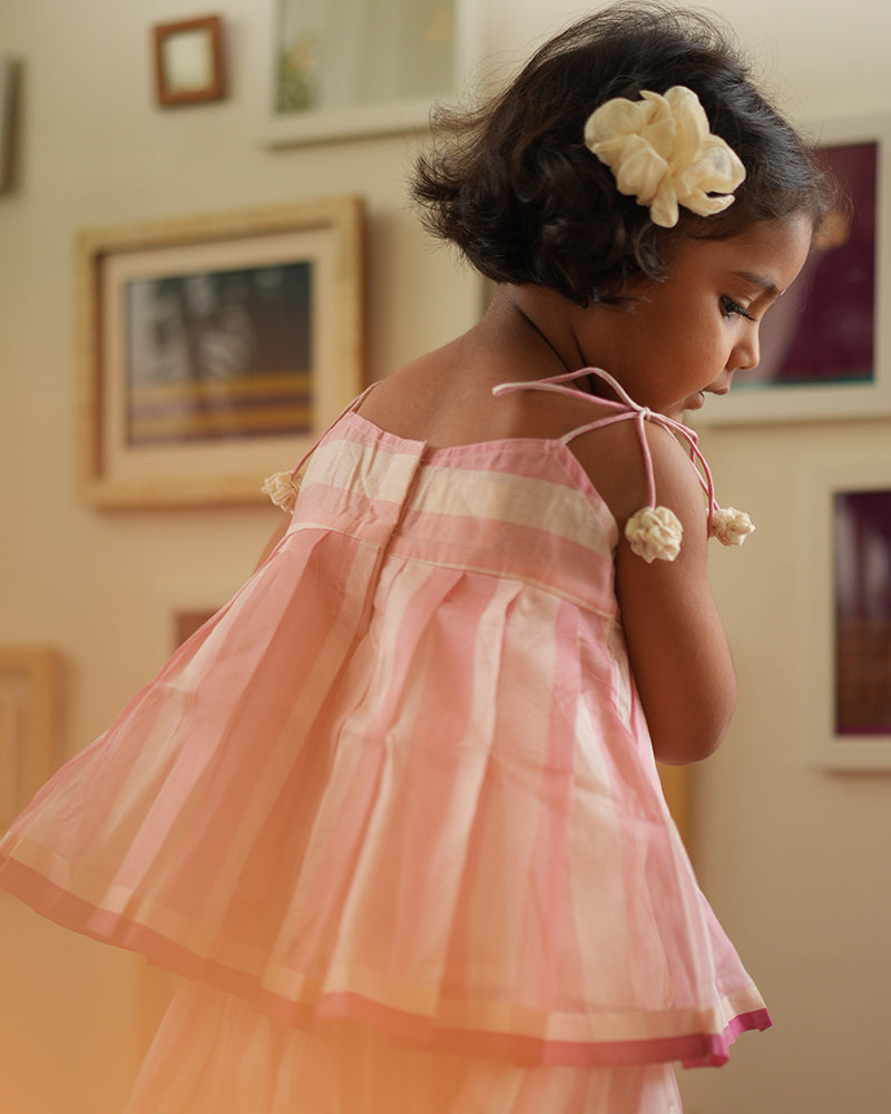 A girl wearing a cute baby pink and white striped cotton silk lehenga handwoven by weavers in Maheshwar, Madhya Pradesh. This Maheshwari Cotton silk lehenga set is perfect for festivities like Navratri, durga pooja, Dussehra, dushehra, diwali pooja, bhai dooj and weddings. Kids ethnic outfits, traditional clothing for kids. Silkwear for kids.