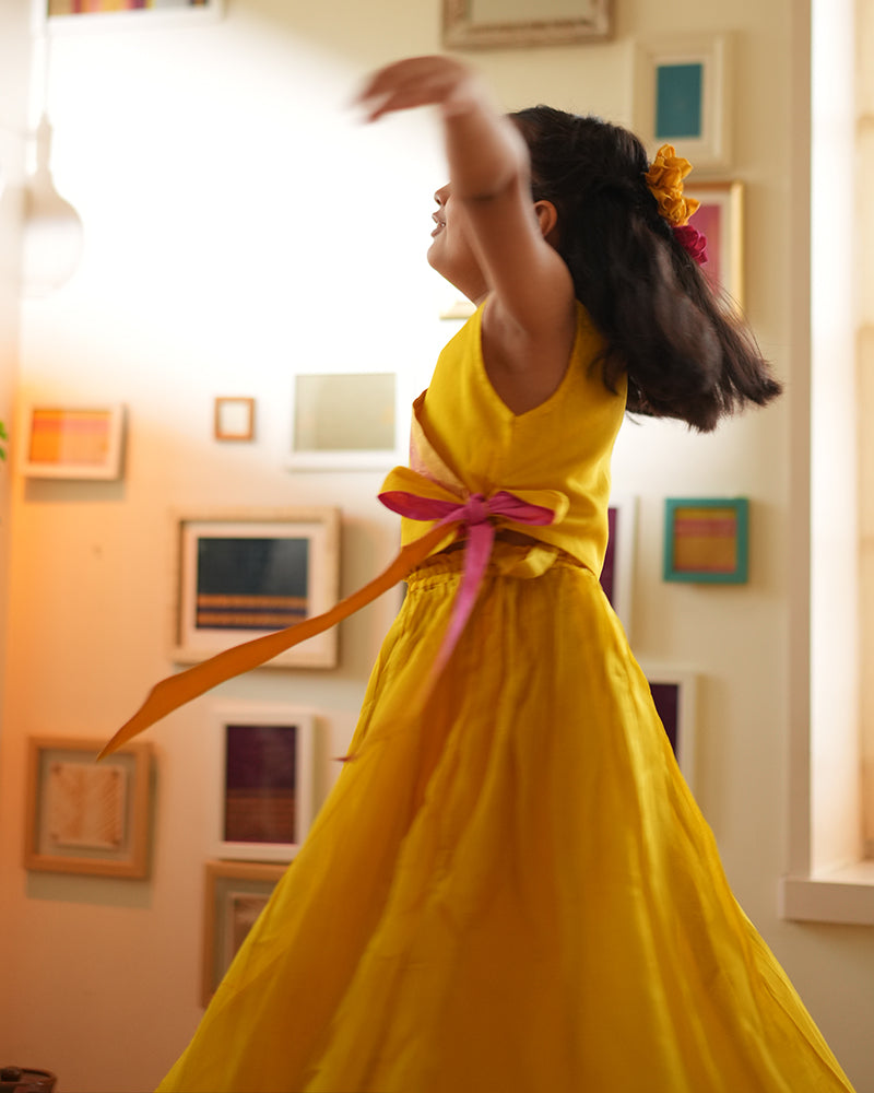 A girl wearing a bright yellow colored cotton silk lehenga handwoven by weavers in Maheshwar, Madhya Pradesh. This Maheshwari Cotton silk lehenga set is perfect for festivities like Navratri, durga pooja, Dussehra, dushehra, diwali pooja, bhai dooj and weddings. Kids ethnic outfits, traditional clothing for kids. Silkwear for kids.