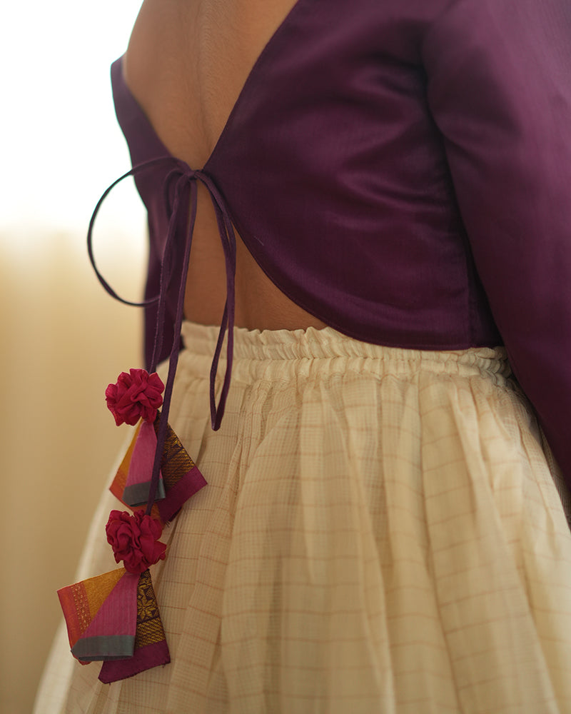 A girl wearing a deep purple wine colored cotton silk blouse with an off white a gold striped lehenga handwoven by weavers in Maheshwar, Madhya Pradesh. Tie back choli
