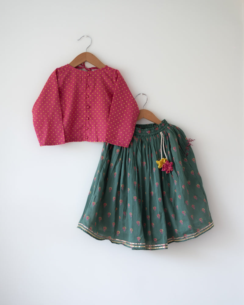A Polka dot magenta pink hand block printed choli blouse with a dark green floral print lehenga set. Festive full sleeves blouse & gota lace skirt with pockets and tassels.