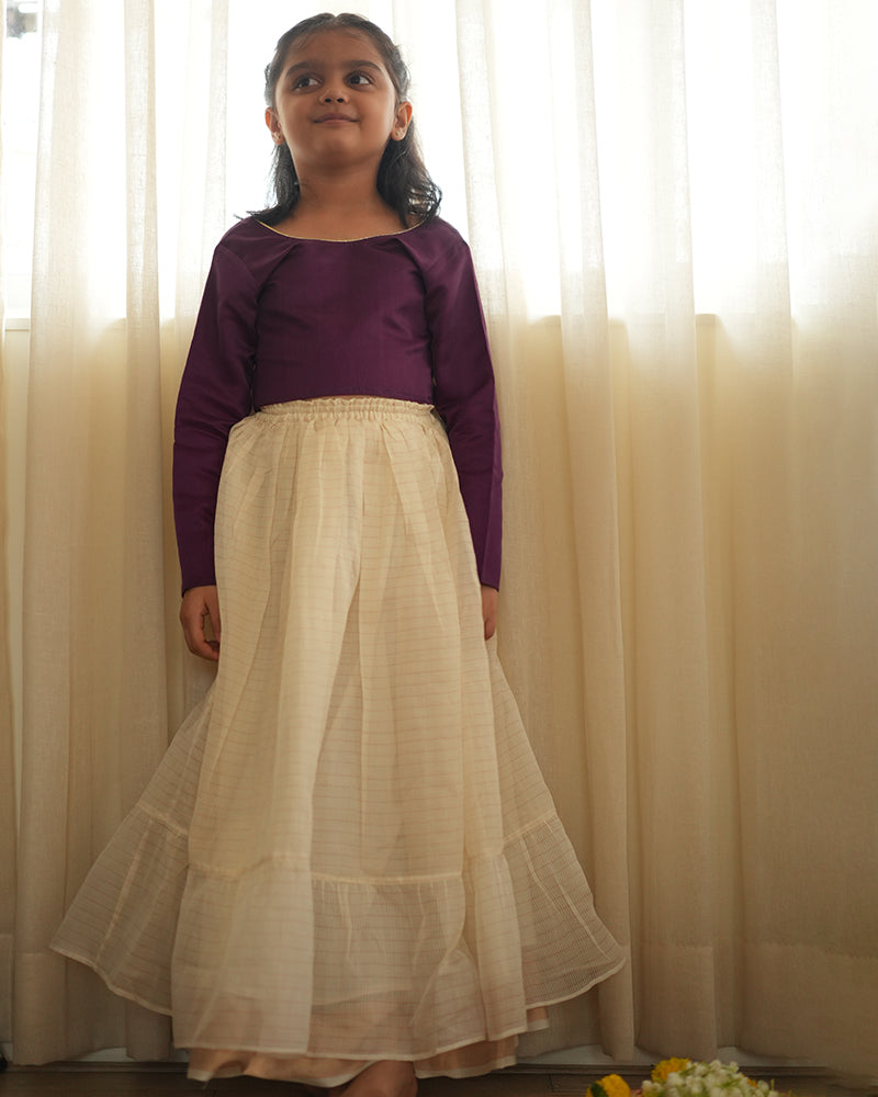 A girl wearing a deep purple wine colored cotton silk blouse with an off white a gold striped lehenga handwoven by weavers in Maheshwar, Madhya Pradesh. This Maheshwari Cotton silk lehenga set is perfect for festivities like Navratri, durga pooja, Dussehra, dushehra, diwali pooja, bhai dooj and weddings. Kids ethnic outfits, traditional clothing for kids. Silkwear for kids. Skirt as dress.