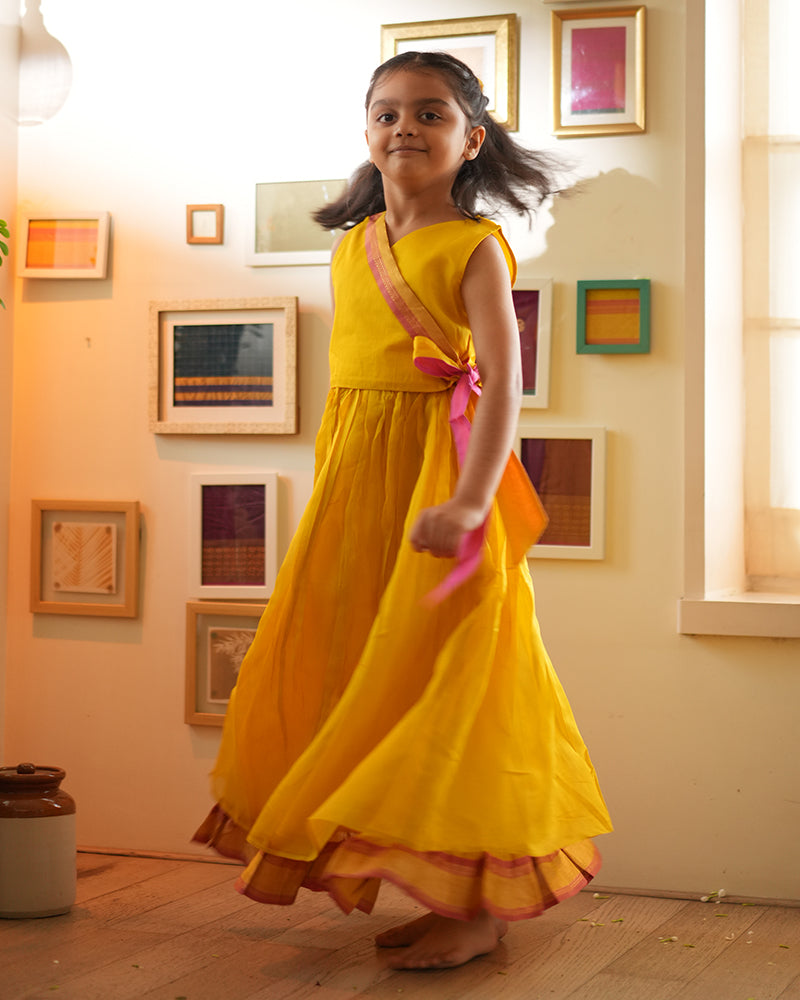 A girl wearing a bright yellow colored cotton silk lehenga handwoven by weavers in Maheshwar, Madhya Pradesh. This Maheshwari Cotton silk lehenga set is perfect for festivities like Navratri, durga pooja, Dussehra, dushehra, diwali pooja, bhai dooj and weddings. Kids ethnic outfits, traditional clothing for kids. Silkwear for kids.