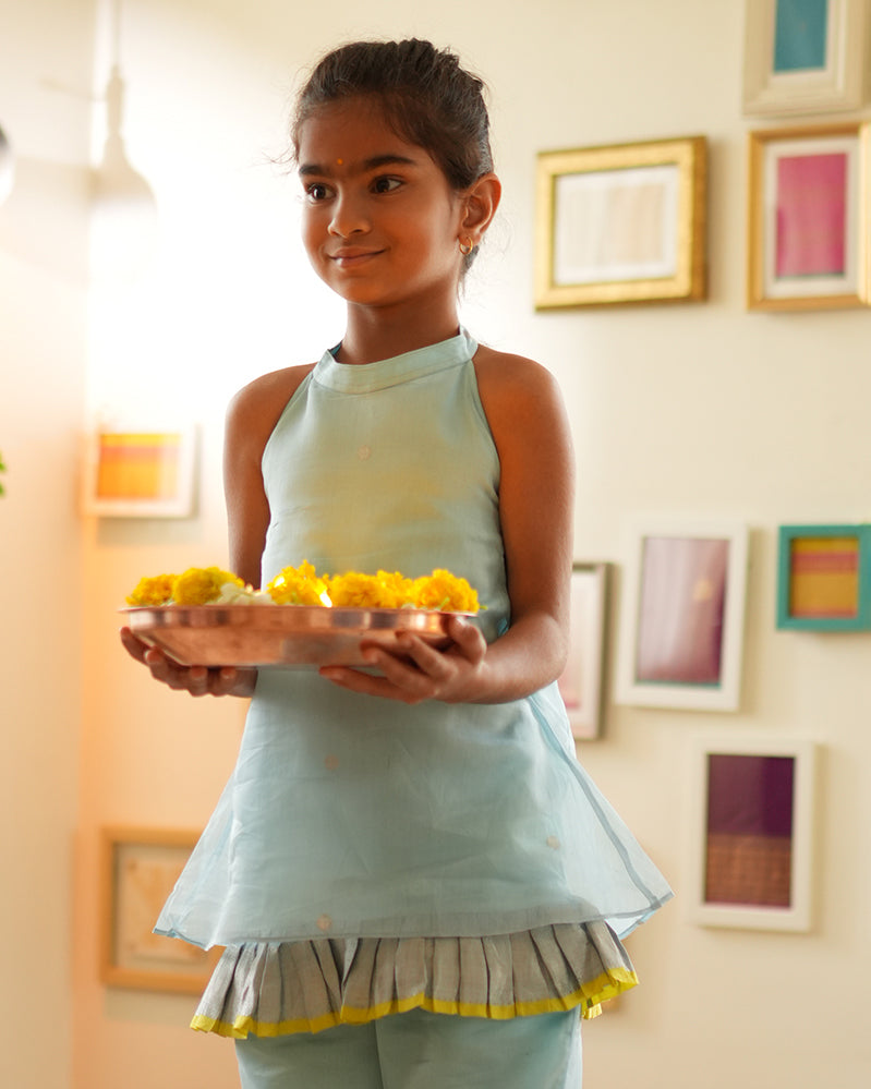 A girl wearing a cute light baby blue and yellow cotton silk sharara suit set handwoven with silver polka dots by weavers in Maheshwar, Madhya Pradesh. Kids ethnic outfits, traditional clothing for kids. Silkwear for kids. Halter neck kurti top, salwar kamiz.