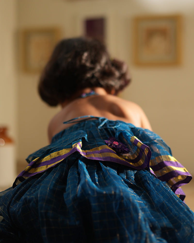 A girl wearing a deep teal blue colored cotton silk lehenga halter choli with golden checks handwoven by weavers in Maheshwar, Madhya Pradesh. This Maheshwari Cotton silk lehenga set is perfect for festivities like Navratri, durga pooja, Dussehra, dushehra, diwali pooja, bhai dooj and weddings. Gathered skirt with a ghera blouse. Kids ethnic outfits, traditional clothing for kids. Silkwear for kids. Ghera skirt