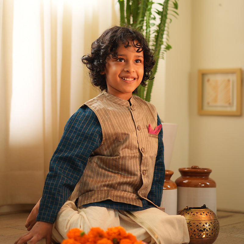 A Boy wearing a steel grey Indian festive bandi nehru jacket with golden stripes made with Handwoven cotton silk fabric woven by artisans in Maheshwar Madhya Pradesh. This kids ethnic kurta is best for upcoming festivities like kids Navratri outfit, kids durga pooja kurta, Dussehra, dushehra, ethnic dress for Diwali, bhai dooj and kids/ boys kurta for weddings. Paired with an off white dhoti/ mundu. Perfect Kids silk wear, ethnic wear for kids, festive clothing for kids.
