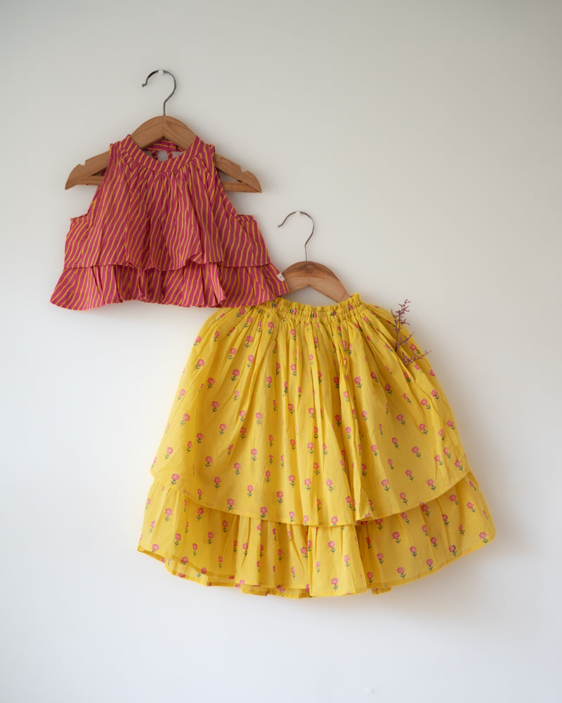 A chevron print lehariya hand block printed top with a bright yellow floral print lehenga. Festive sleeveless blouse & layered skirt with pockets set.