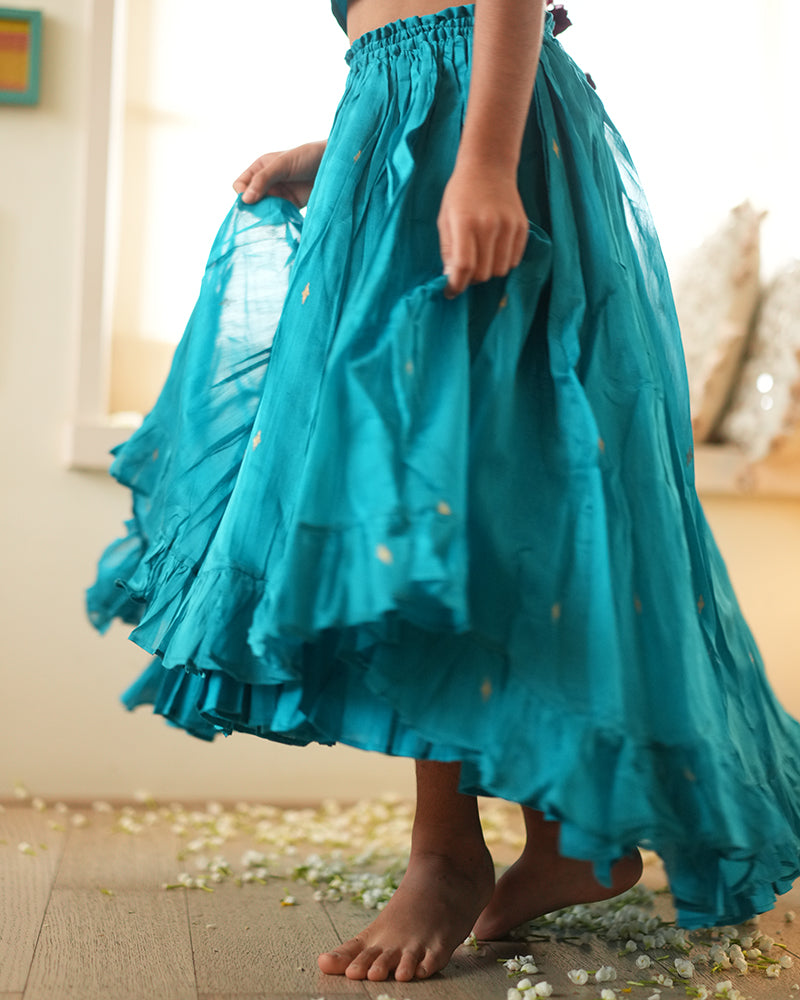 A girl wearing a bright turquoise blue colored cotton silk lehenga choli with golden buttis handwoven by weavers in Maheshwar, Madhya Pradesh. This Maheshwari Cotton silk lehenga set is perfect for festivities like Navratri, durga pooja, Dussehra, dushehra, diwali pooja, bhai dooj and weddings. High low skirt.