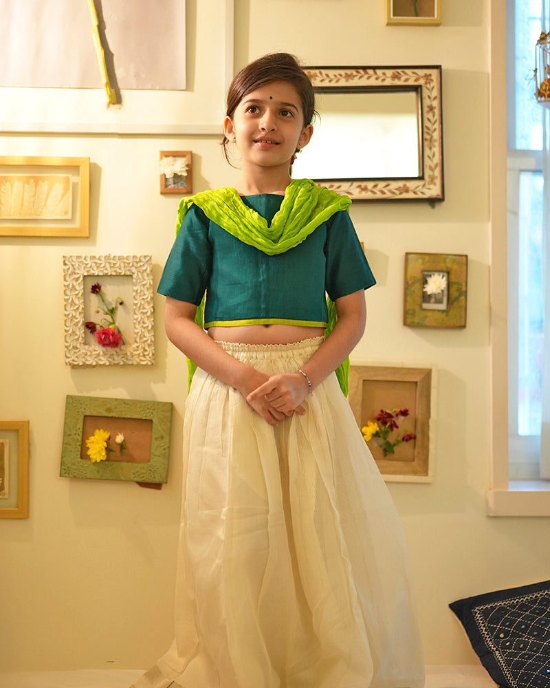 Little girl in Diwali or Onam dress in green choli white lehenga with a dupatta and bindi standing and smiling for the camera.