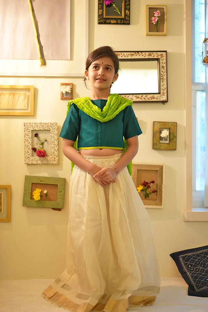 Little girl in Diwali or Onam dress in green choli white lehenga with a dupatta and bindi standing and smiling for the camera. 