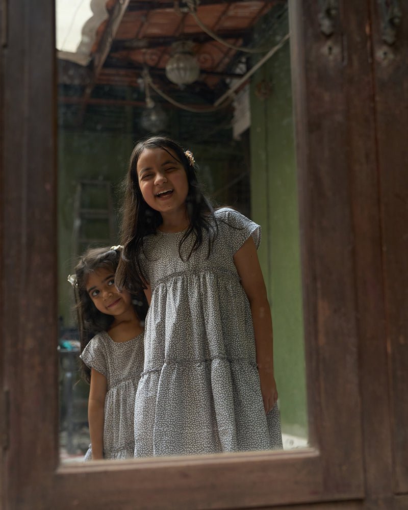 baby-girls-looking-at-themselves-in-the-mirror-dressed-in-matching-clothes-wearing-lovetheworldtodays-tiered-dress-in-grey-hand-block-print