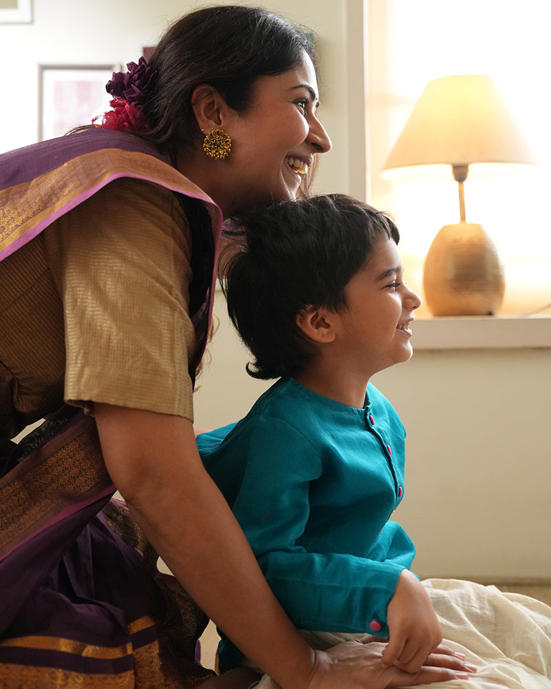 A Boy wearing a bright turquoise blue Indian festive Kurta with golden butti motifs made with Handwoven cotton silk fabric woven by artisans in Maheshwar Madhya Pradesh. Mom & boy bonding over diwali. Family celebrating diwali. Mom & Son duo.