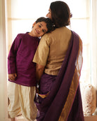 A Boy wearing a deep purple violet Indian festive Kurta with side buttons made with Handwoven cotton silk fabric woven by artisans in Maheshwar Madhya Pradesh. This kids ethnic kurta is best for upcoming festivities like kids Navratri outfit, kids durga pooja kurta, Dussehra, dushehra, ethnic dress for Diwali, bhai dooj and kids/ boys kurta for weddings. Paired with an off white dhoti/ mundu. Perfect Kids silk wear, ethnic wear for kids, festive clothing for kids. Mom son duo. 
