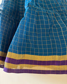 A deep teal blue sleeveless tiered dress with golden checks for infants in handwoven cotton silk by artisans in Maheshwar Madhya Pradesh. Perfect for festivities like Navratri, diwali, Dussehra, dushehra, bhai dooj. Infant wear. Baby ethnic wear. Silkwear for babies. Baby girl festive wear. Dress with border. 