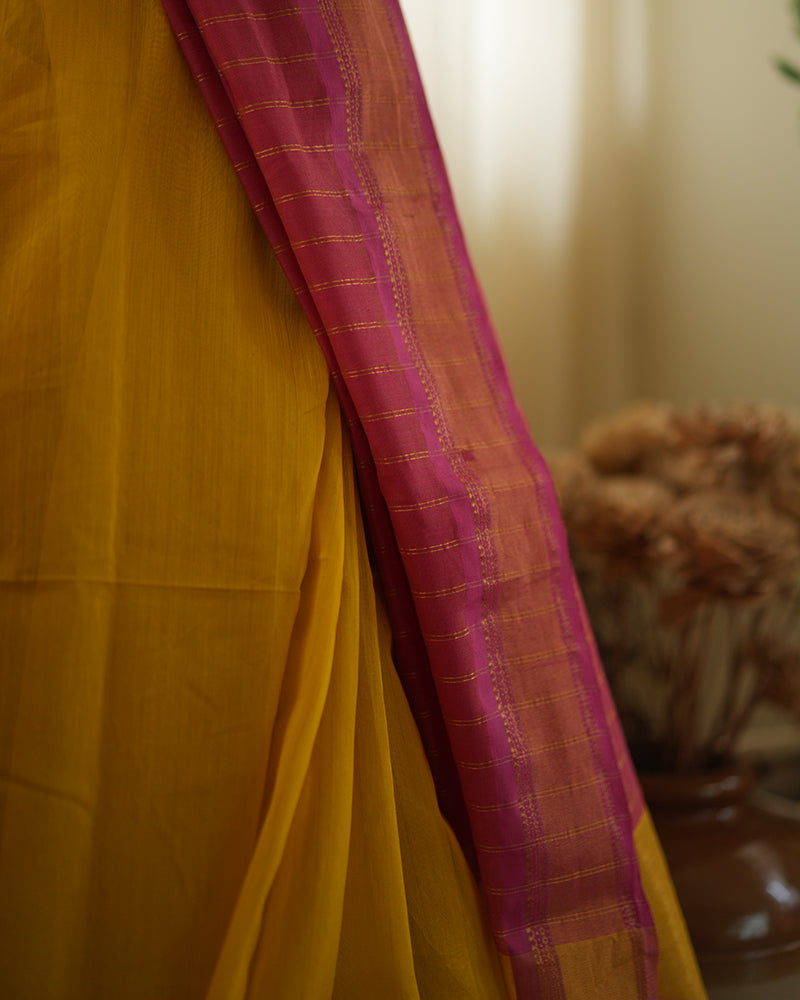 A woman wearing a bright yellow colored cotton silk saree with a pink and gold border and pallu with pink and gold stripes handwoven by weavers in Maheshwar, Madhya Pradesh. Women's silk wear, silk saree for women, cotton silk saree, heavy pallu sarees. 