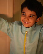 A Boy wearing a light sky blue Indian festive Kurta with golden polka dots motifs made with Handwoven cotton silk fabric woven by artisans in Maheshwar Madhya Pradesh. Perfect Kids silk wear, ethnic wear for kids, festive clothing for kids.