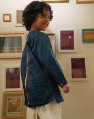 A Boy wearing a dark teal blue Indian festive Kurta with golden checks made with Handwoven cotton silk fabric woven by artisans in Maheshwar Madhya Pradesh. This kids ethnic kurta is best for upcoming festivities like kids Navratri outfit, kids durga pooja kurta, Dussehra, dushehra, ethnic dress for Diwali, bhai dooj and kids/ boys kurta for weddings. Paired with an off white dhoti/ mundu. Perfect Kids silk wear, ethnic wear for kids, festive clothing for kids.