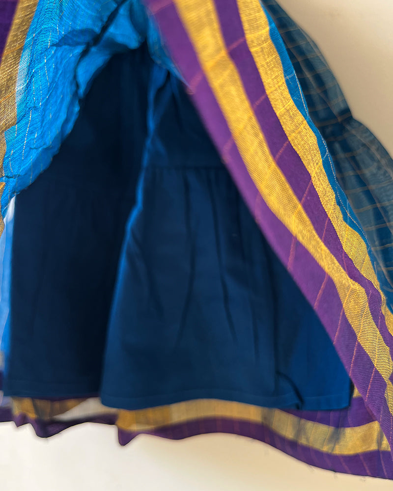 A deep teal blue sleeveless tiered dress with golden checks for infants in handwoven cotton silk by artisans in Maheshwar Madhya Pradesh. Perfect for festivities like Navratri, diwali, Dussehra, dushehra, bhai dooj. Infant wear. Baby ethnic wear. Silkwear for babies. Baby girl festive wear. Baby dress with lining. 