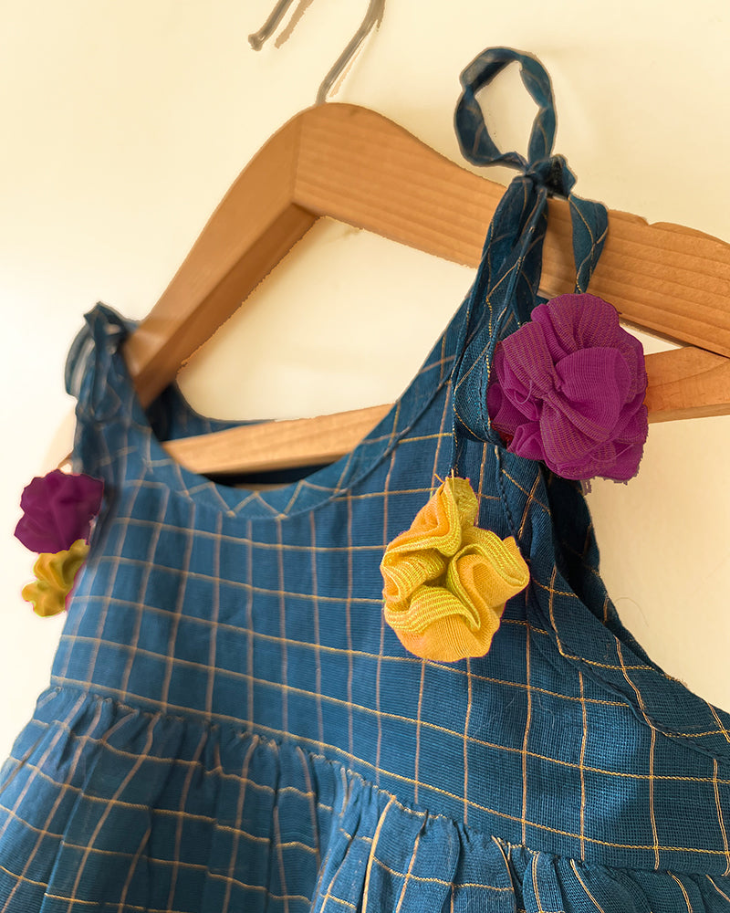 A deep teal blue sleeveless tiered dress with golden checks for infants in handwoven cotton silk by artisans in Maheshwar Madhya Pradesh. Perfect for festivities like Navratri, diwali, Dussehra, dushehra, bhai dooj. Infant wear. Baby ethnic wear. Silkwear for babies. Baby girl festive wear. Dress with tassels.