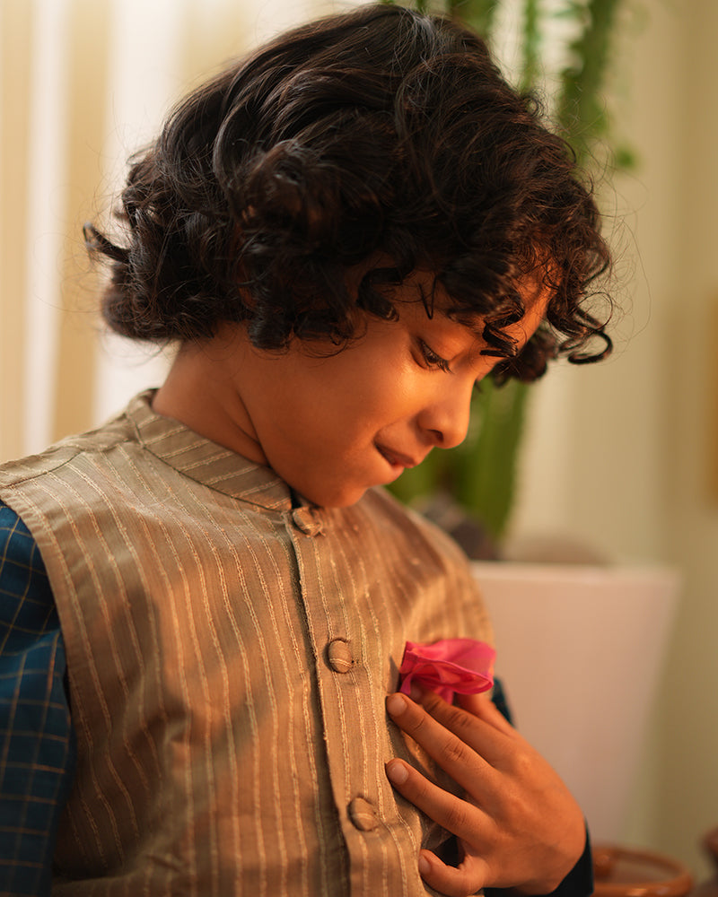 A Boy wearing a steel grey Indian festive bandi nehru jacket with golden stripes made with Handwoven cotton silk fabric woven by artisans in Maheshwar Madhya Pradesh. 
