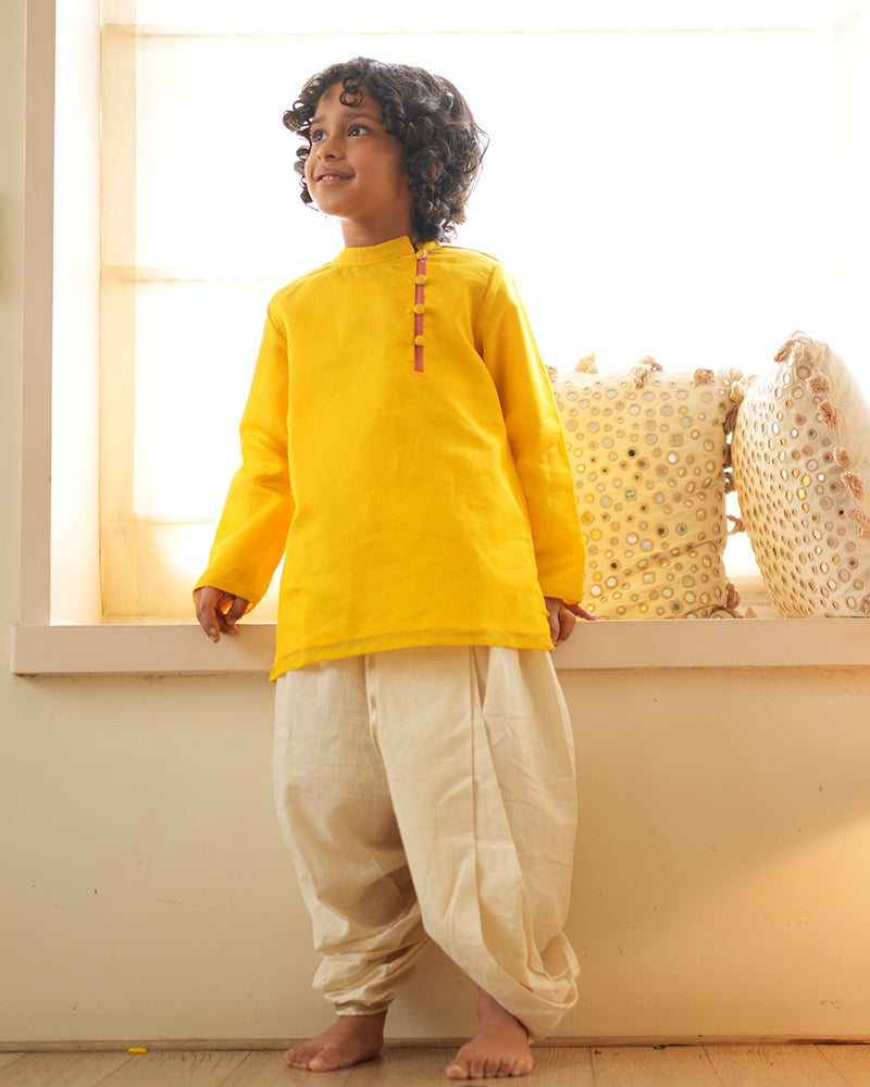 A Boy wearing a bright yellow Indian festive Kurta with side buttons made with Handwoven cotton silk fabric woven by artisans in Maheshwar Madhya Pradesh. This kids ethnic kurta is best for upcoming festivities like kids Navratri outfit, kids durga pooja kurta, Dussehra, dushehra, ethnic dress for Diwali, bhai dooj and kids/ boys kurta for weddings. Paired with an off white dhoti/ mundu. Perfect Kids silk wear, ethnic wear for kids, festive clothing for kids.