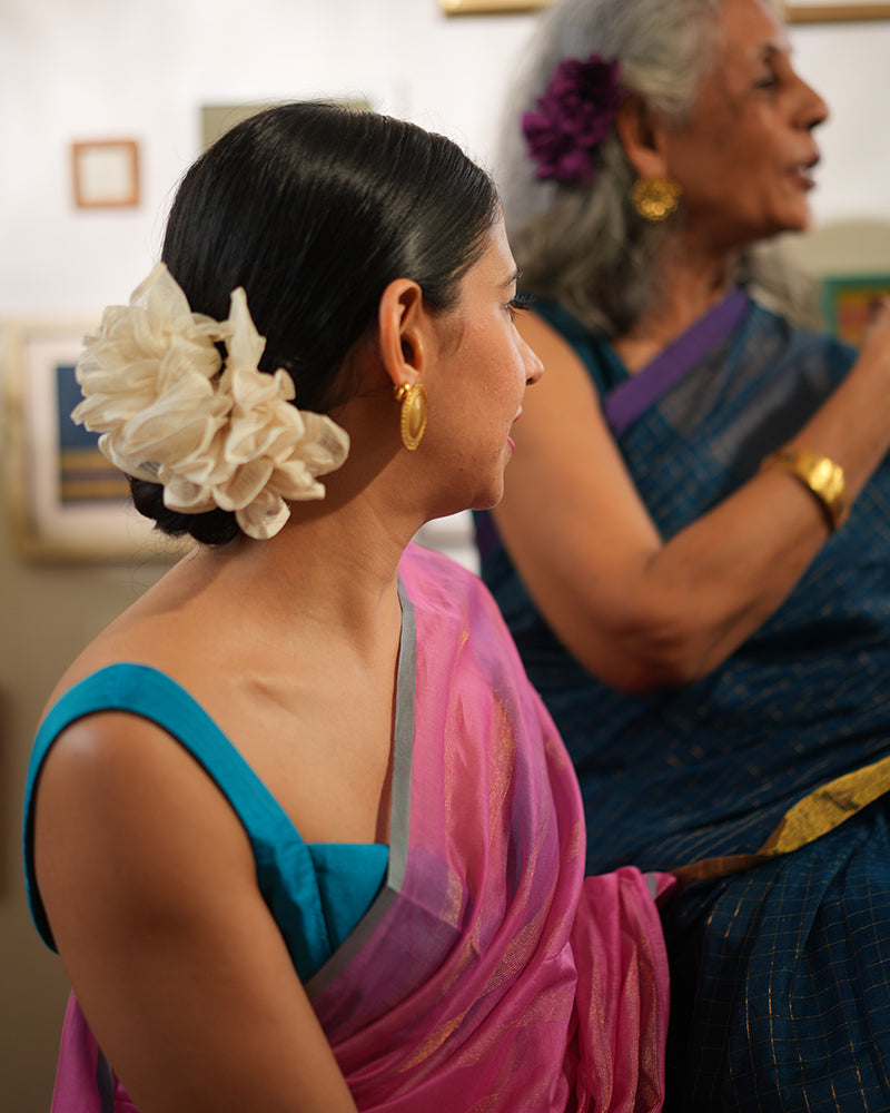 A woman wearing a bright pink colored cotton silk saree with a blue border and golden stripes handwoven by weavers in Maheshwar, Madhya Pradesh.
