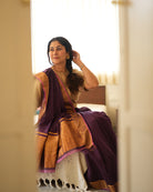 A woman wearing a deep purple wine colored cotton silk saree handwoven by weavers in Maheshwar, Madhya Pradesh. This Maheshwari Cotton silk saree is perfect for festivities like Navratri, durga pooja, Dussehra, dushehra, diwali pooja, bhai dooj and weddings. Paired with a golden blouse. Women's silk wear, silk saree for women, cotton silk saree, heavy pallu border sarees. 
