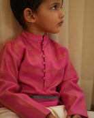 A Boy wearing a bright rani Pink Indian festive Kurta with thick golden stripes made with Handwoven cotton silk fabric woven by artisans in Maheshwar Madhya Pradesh.
