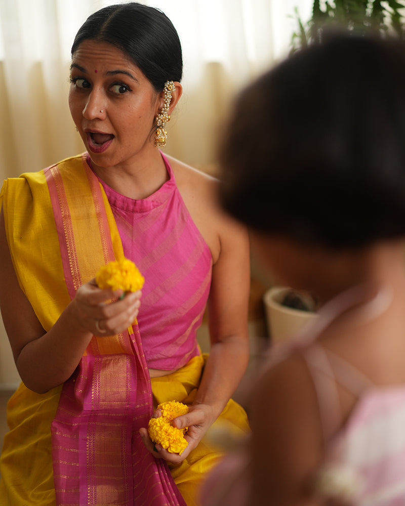 A woman wearing a bright yellow colored cotton silk saree with a pink and gold border and pallu with pink and gold stripes handwoven by weavers in Maheshwar, Madhya Pradesh. This Maheshwari Cotton silk saree is perfect for festivities like Navratri, durga pooja, Dussehra, dushehra, diwali pooja, bhai dooj and weddings. Women's silk wear, silk saree for women, cotton silk saree, heavy pallu sarees. 