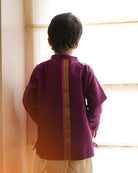 A Boy wearing a deep purple violet Indian festive Kurta with side buttons made with Handwoven cotton silk fabric woven by artisans in Maheshwar Madhya Pradesh. This kids ethnic kurta is best for upcoming festivities like kids Navratri outfit, kids durga pooja kurta, Dussehra, dushehra, ethnic dress for Diwali, bhai dooj and kids/ boys kurta for weddings. Paired with an off white dhoti/ mundu. Perfect Kids silk wear, ethnic wear for kids, festive clothing for kids.