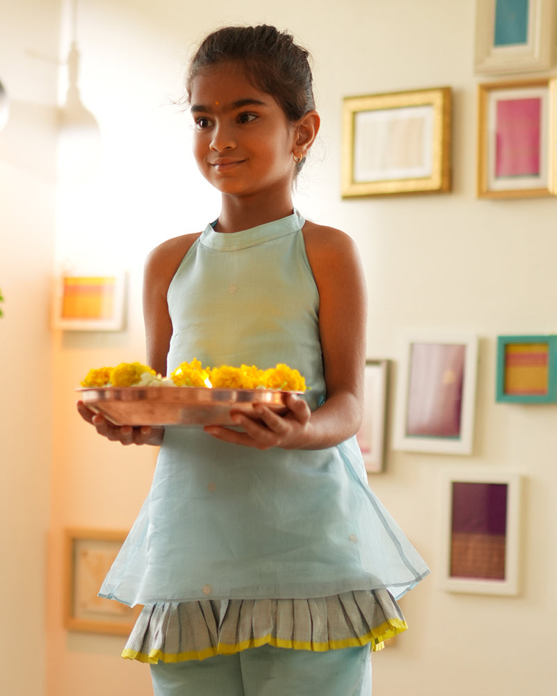 A girl wearing a cute light baby blue and yellow cotton silk sharara suit set handwoven with silver polka dots by weavers in Maheshwar, Madhya Pradesh. Kids ethnic outfits, traditional clothing for kids. Silkwear for kids. Halter neck kurti top, salwar kamiz. 