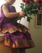 A girl wearing a cute deep purple violet cotton silk sharara suit set handwoven with golden border by weavers in Maheshwar, Madhya Pradesh. This Maheshwari Cotton silk suit set is perfect for festivities like Navratri, durga pooja, Dussehra, dushehra, diwali pooja, bhai dooj and weddings. Kids ethnic outfits, traditional clothing for kids. Silkwear for kids. Sharara set, suit set, salwar set for girls. 