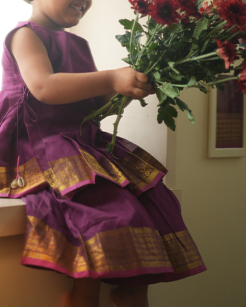 A girl wearing a cute deep purple violet cotton silk sharara suit set handwoven with golden border by weavers in Maheshwar, Madhya Pradesh. This Maheshwari Cotton silk suit set is perfect for festivities like Navratri, durga pooja, Dussehra, dushehra, diwali pooja, bhai dooj and weddings. Kids ethnic outfits, traditional clothing for kids. Silkwear for kids. Sharara set, suit set, salwar set for girls. 