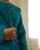 A Boy wearing a bright turquoise blue Indian festive Kurta with golden butti motifs made with Handwoven cotton silk fabric woven by artisans in Maheshwar Madhya Pradesh. 