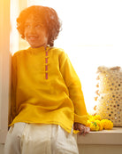 A Boy wearing a bright yellow Indian festive Kurta with side buttons made with Handwoven cotton silk fabric woven by artisans in Maheshwar Madhya Pradesh.