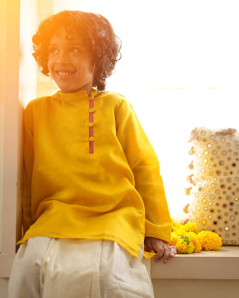 A Boy wearing a bright yellow Indian festive Kurta with side buttons made with Handwoven cotton silk fabric woven by artisans in Maheshwar Madhya Pradesh.