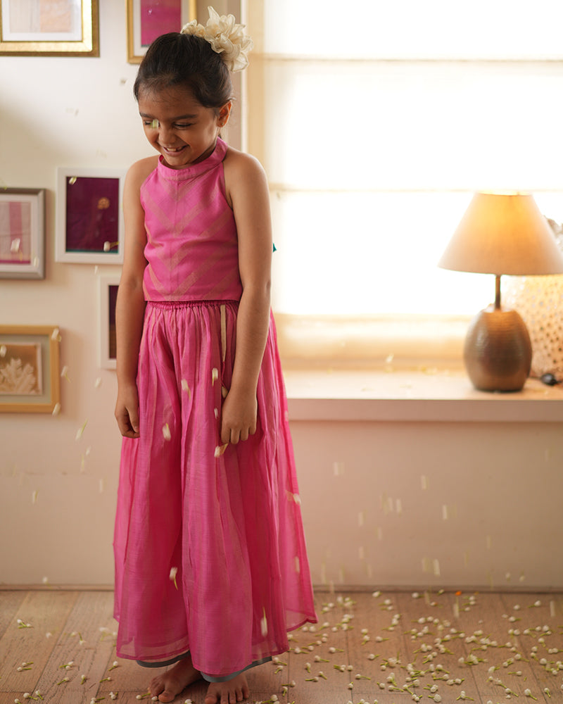 A girl wearing a cute pink and golden striped cotton silk coord set handwoven with silver polka dots by weavers in Maheshwar, Madhya Pradesh. This Maheshwari Cotton silk suit set is perfect for festivities like Navratri, durga pooja, Dussehra, dushehra, diwali pooja, bhai dooj and weddings. Kids ethnic outfits, traditional clothing for kids. Silkwear for kids. Halter neck top with pallazo. Pallazo pants. Coord set. 