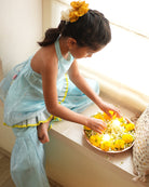 A girl wearing a cute light baby blue and yellow cotton silk sharara suit set handwoven with silver polka dots by weavers in Maheshwar, Madhya Pradesh. This Maheshwari Cotton silk suit set is perfect for festivities like Navratri, durga pooja, Dussehra, dushehra, diwali pooja, bhai dooj and weddings. Kids ethnic outfits, traditional clothing for kids. Silkwear for kids. Halter neck kurti top, salwar kamiz. 