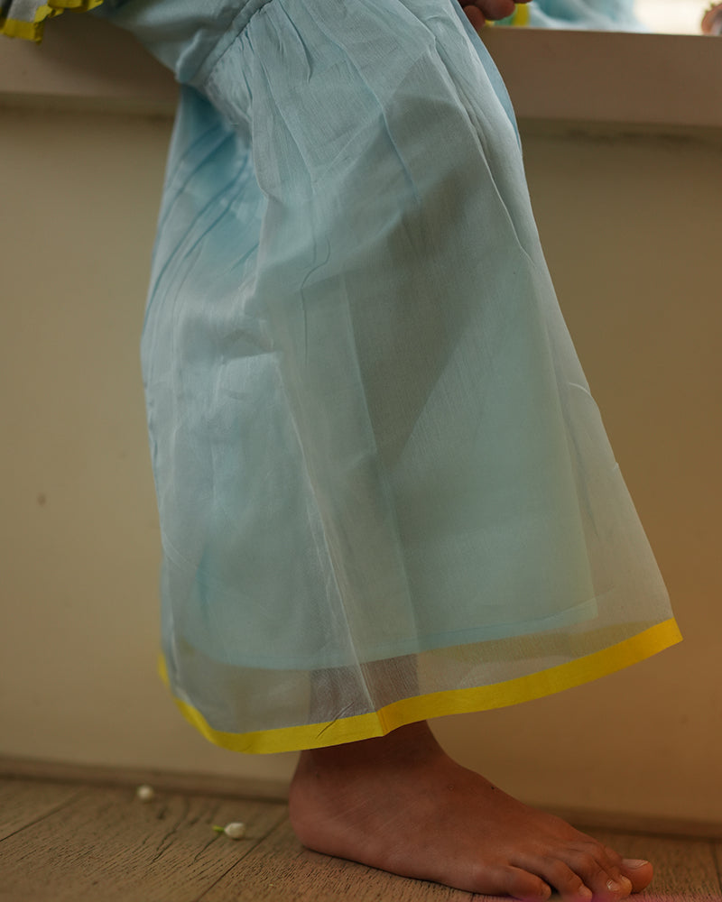 A girl wearing a cute light baby blue and yellow cotton silk sharara suit set handwoven with silver polka dots by weavers in Maheshwar, Madhya Pradesh. Silkwear for kids. Halter neck kurti top, salwar kamiz. Sharara pant. 